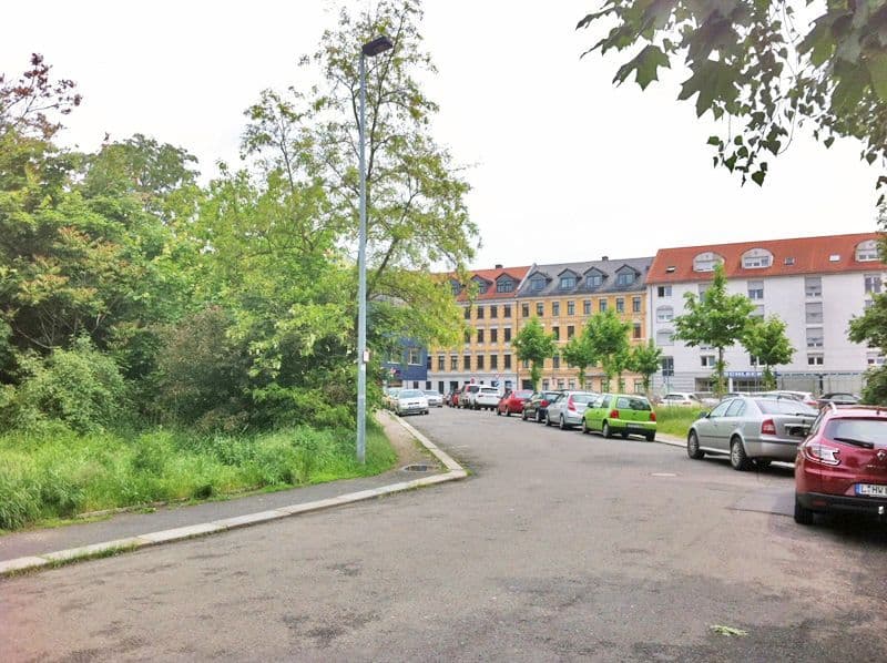 Parkplatz mit geparkten Autos, dahinter gelbe und weiße Gründerzeitbauten mit Mansarddächern, Schreiberstraße in Leipzig