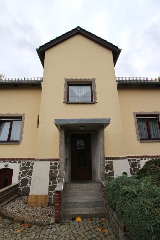 Zweigeschossiges Haus mit Satteldach, beige Fassade, Natursteinsockel, zentraler Eingang mit Vordach