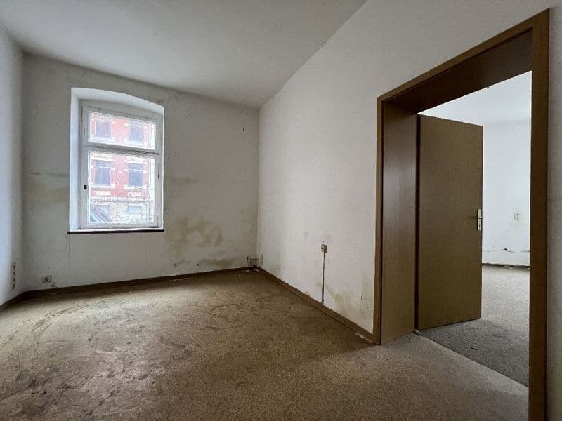 Leerer Raum mit Betonboden, weiße Wände, Fenster zur Straße, offene Tür mit dunklem Holzrahmen