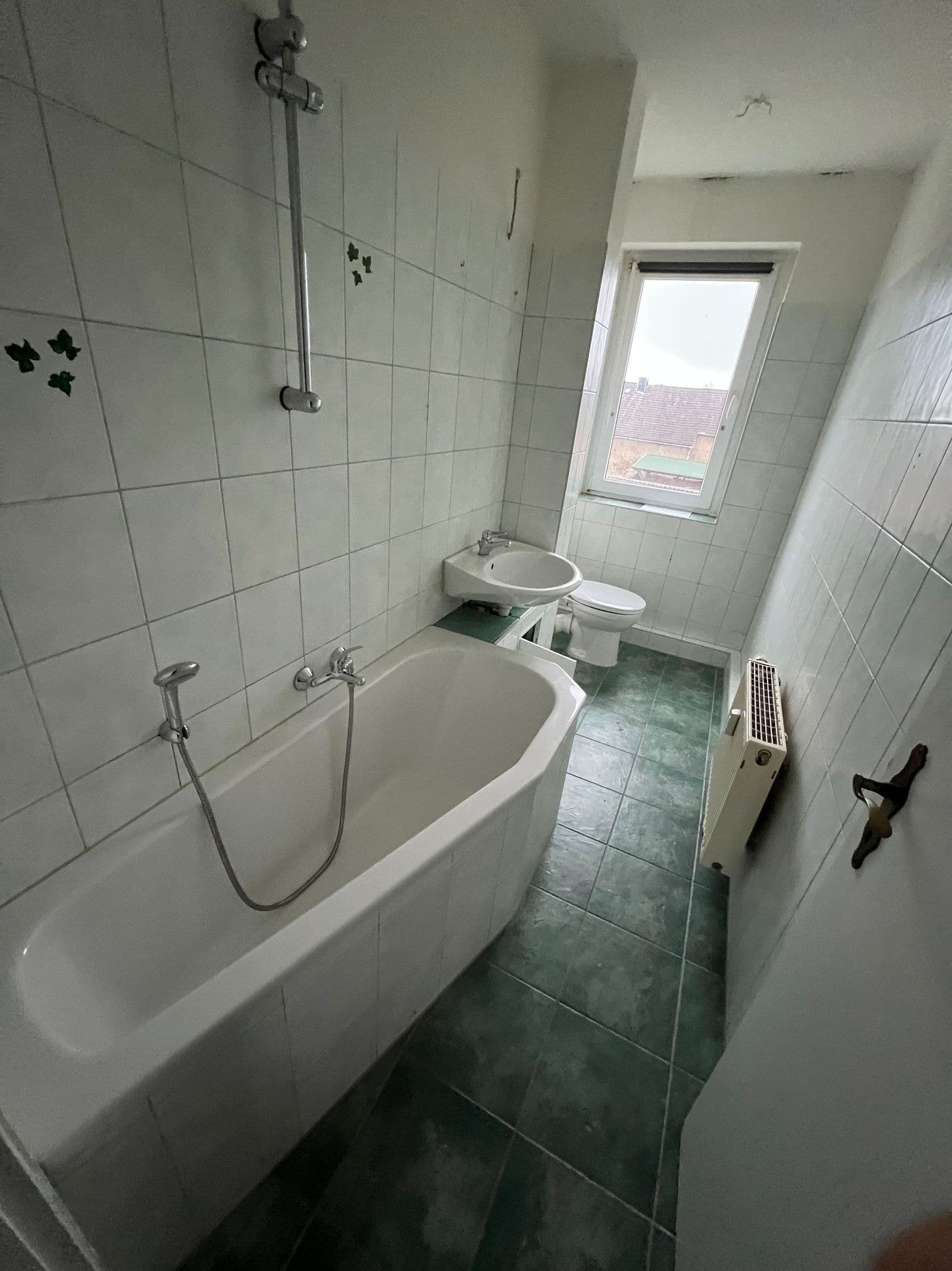 Schmales Badezimmer mit Wanne, Bidet, Toilette, weiße Wandfliesen, grüner Fliesenboden, Fenster