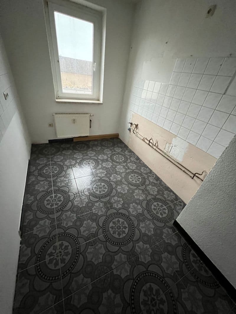 Leeres Badezimmer mit gemustertem Fliesenboden, weißen Wandfliesen, Heizkörper und Fenster