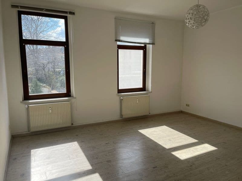 Leeres Zimmer mit Parkettboden, zwei Fenster mit Heizkörpern, Pendelleuchte