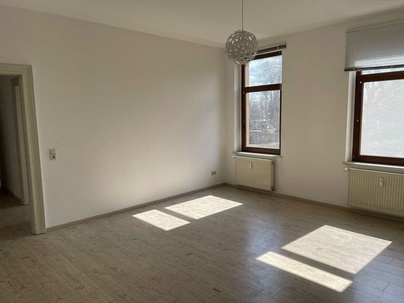 Leerer Wohnraum mit Holzparkett, zwei Fenster mit Holzrahmen, Heizkörper, hängende Kugelleuchte