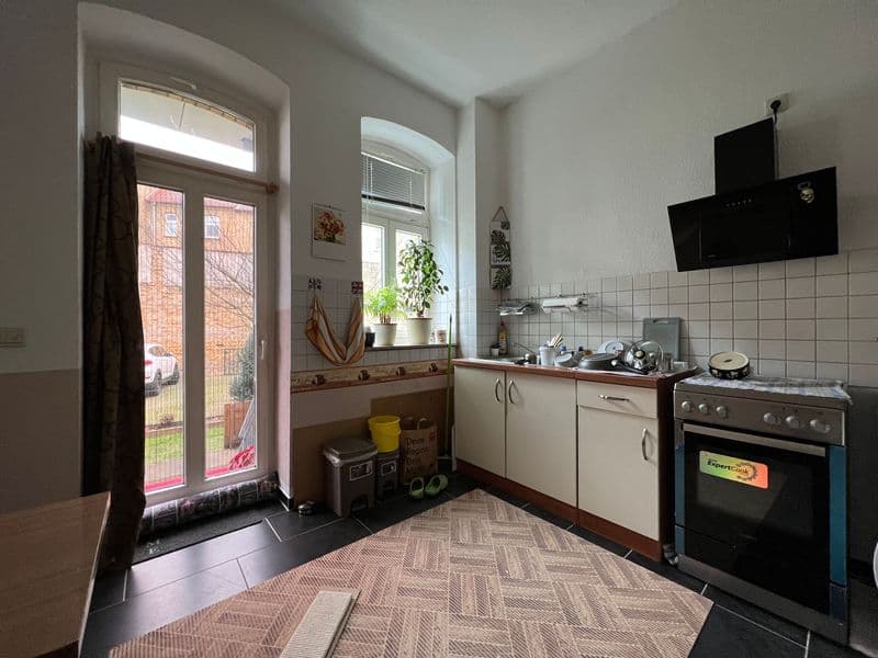 Küche mit weißen Schränken, Fliesenspiegel, schwarzem Herd, Fenster zur Terrasse mit Glastür
