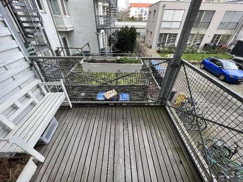 Balkon mit Holzbelag, Metallgeländer und Pflanzenkübeln, Blick auf Parkplatz und Wohngebäude