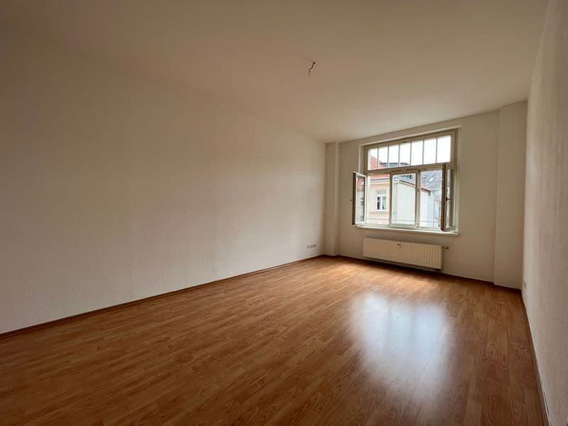 Leeres Zimmer mit Parkettboden, helle Wände, großes Fenster mit Oberlicht, Heizkörper