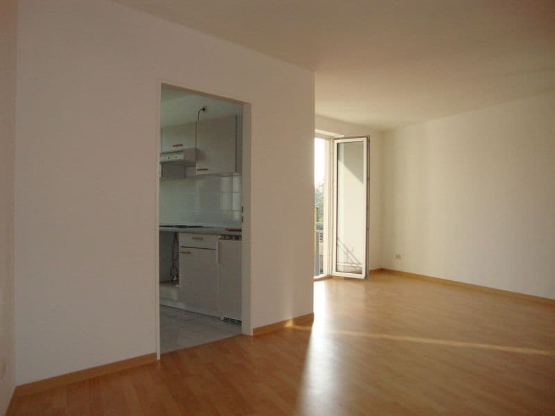 Wohnraum mit Parkettboden, offene Küche mit weißen Fronten, Glasschiebetür zu Balkon