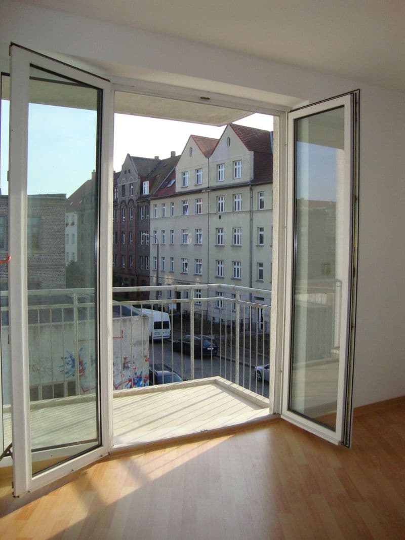 Offene Balkontür mit Blick auf mehrgeschossige Gründerzeitfassaden, Holzparkett im Innenraum