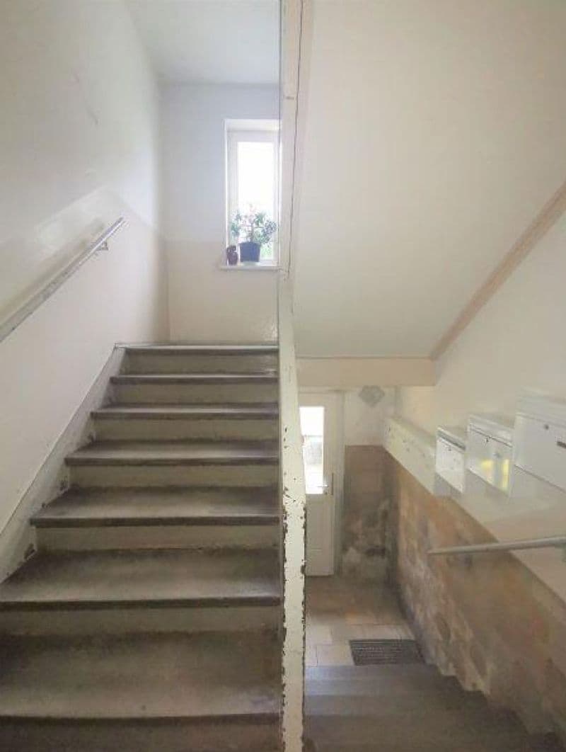 Treppenhaus mit Betontreppe, weißen Wänden, Handlauf links, Fenster oben mit Tageslicht