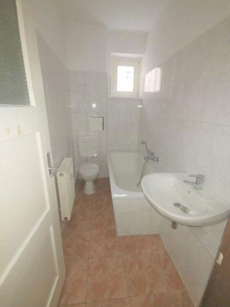 Schmales Badezimmer mit Waschtisch, Toilette, Badewanne mit Duschvorhangstange, Fliesenverkleidung und Fenster