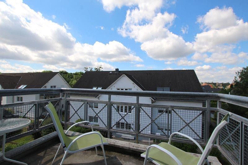 Blick von einer Dachterrasse mit Metallgeländer auf benachbarte zweigeschossige Wohnhäuser mit weißer Fassade und dunklen