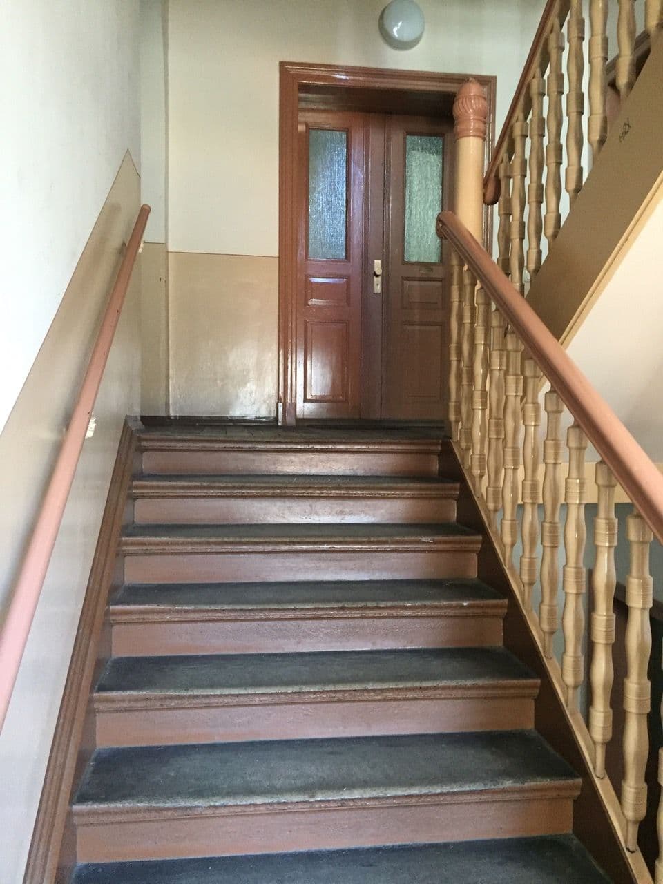 Treppenhaus mit Holztreppe, Handläufen aus Holz und Ziegeltapete an der Wand, Tür mit Glaseinsätzen oben