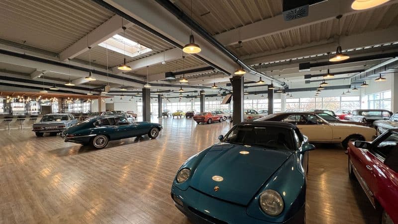 Große Lagerhalle mit Holzdecke, Stahlträgern und Oberlichtern, Parkettboden, mehrere Vintage-Autos ausgestellt