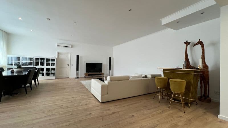 Offenes Wohnzimmer mit Holzparkett, Polstersofa, Flachbildschirm, weißer Kassettendecke, Essbereich mit schwarzem Tisch links