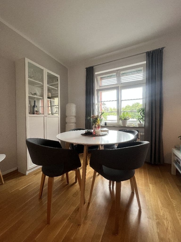 Esszimmer mit rundem weißem Tisch, zwei schwarzen Stühlen, Parkettboden