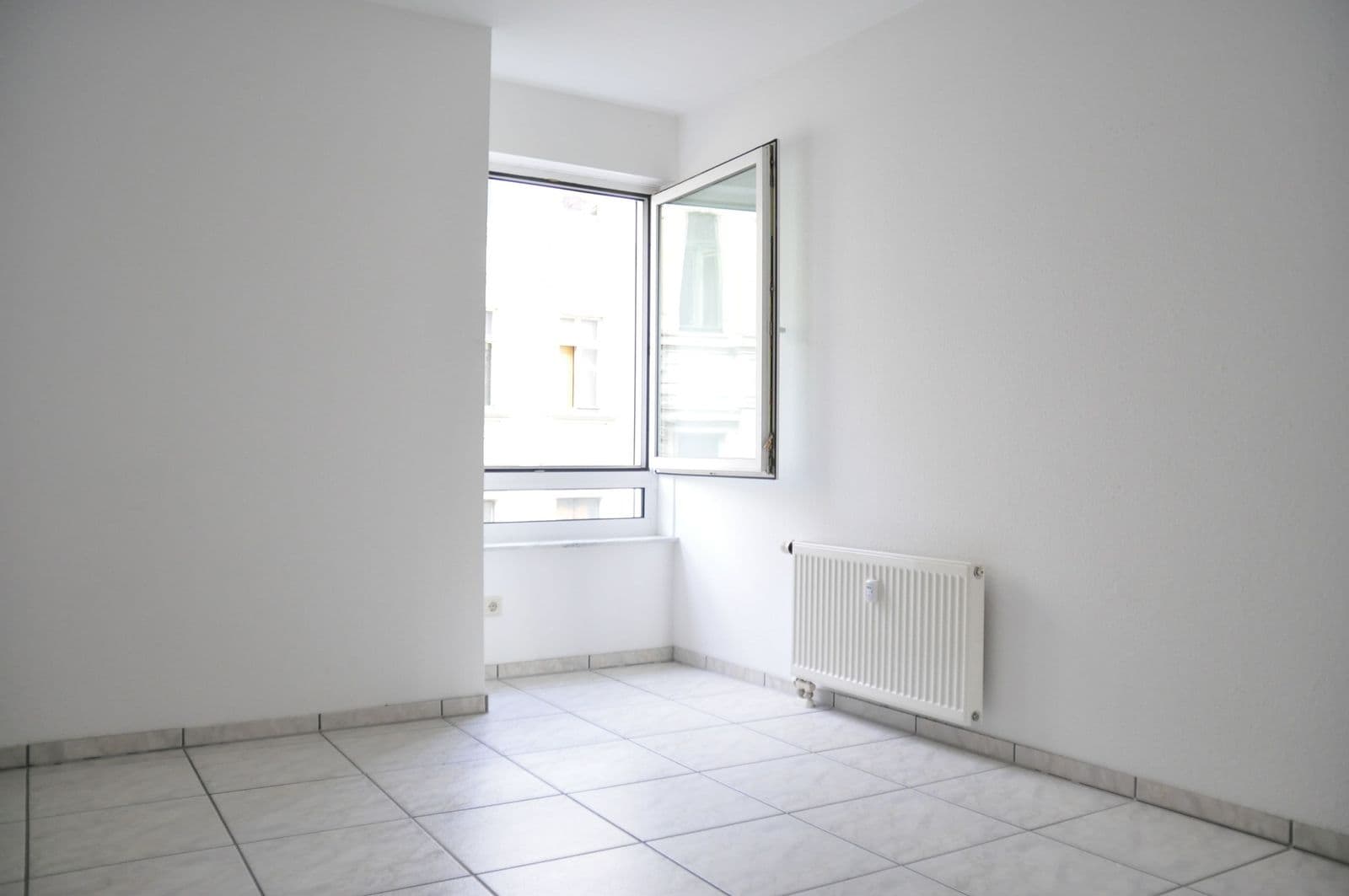 Leeres Zimmer mit Fliesenboden, weiße Wände, Heizkörper, geöffnetes Fenster