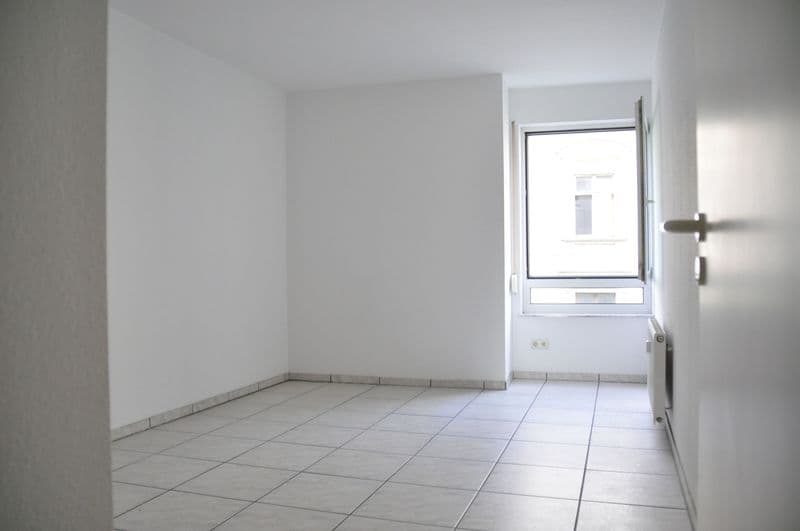 Leerer Wohnraum mit Fliesenboden, hellen Wänden, Fenster und Tür zur Loggia