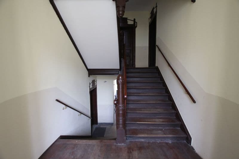 Treppenaufgang mit dunklem Holzgeländer und Stufen, helle Wände, oben Oberlicht