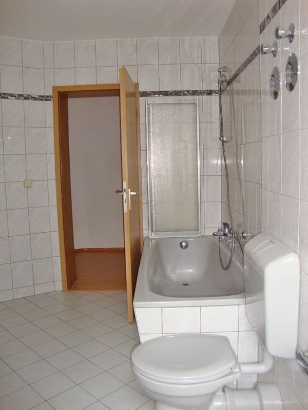 Badezimmer mit weißer Fliesenverkleidung, Wanne mit Duschkabine, Toilette und Holztür