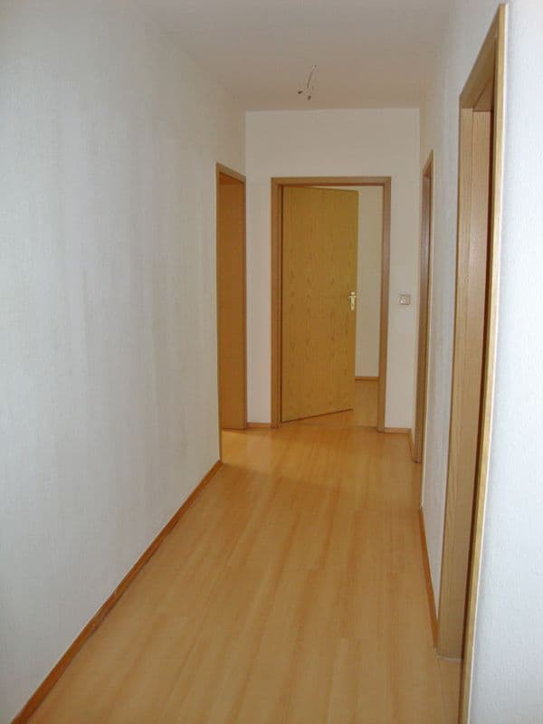 Langer Flur mit Holzparkett, weiße Wände, mehrere Holztüren, helle Decke