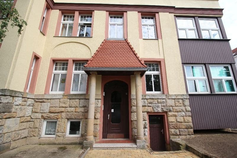 Mehrgeschossiges Wohnhaus mit Fassade aus Putz und Naturstein, roten Fensterrahmen, Dantestraße in Leipzig
