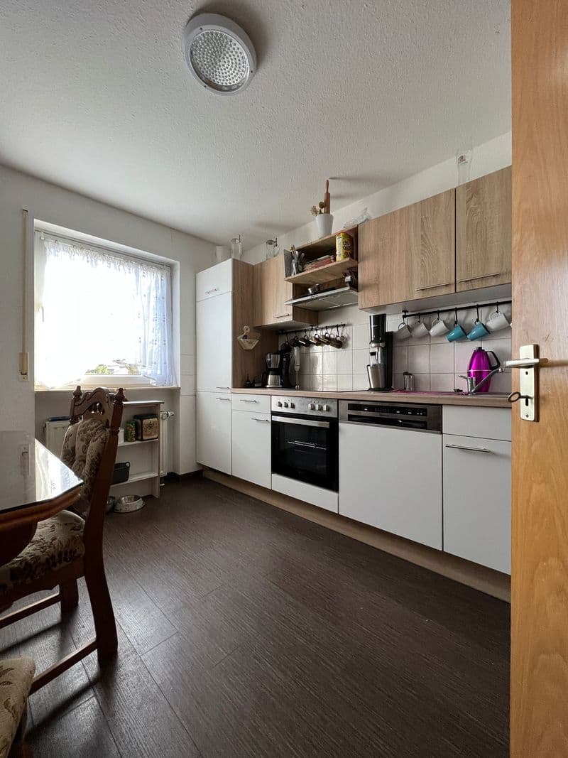 Küche mit weißen und Holzfronten, Einbaugeräte, offene Regale, Fenster mit Blick nach außen, dunkler Bodenbelag