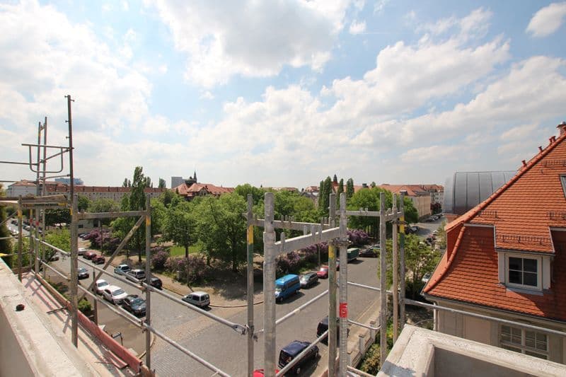 Blick von einer Baustelle auf Parkplatz mit Bäumen und Wohnhäuser mit Ziegeldächern, Ehrensteinstraße in Leipzig-Gohlis-Süd