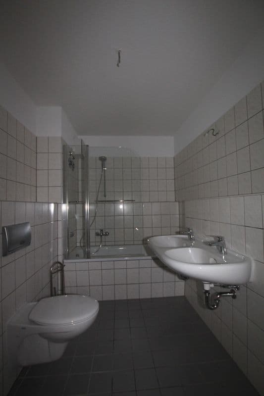 Badezimmer mit weißen Wandfliesen, schwarzem Fliesenboden, Dusche mit Glastür, Doppelwaschbecken und Toilette