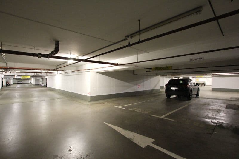 Tiefgarage mit Betonboden, Parkplatzmarkierungen, weißen Stützpfeilern und schwarzen Deckenbalken