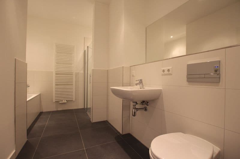Badezimmer mit beigefliesen Wänden, dunklem Fliesenboden, Waschbecken, WC, Handtuchheizung und bodengleicher Dusche