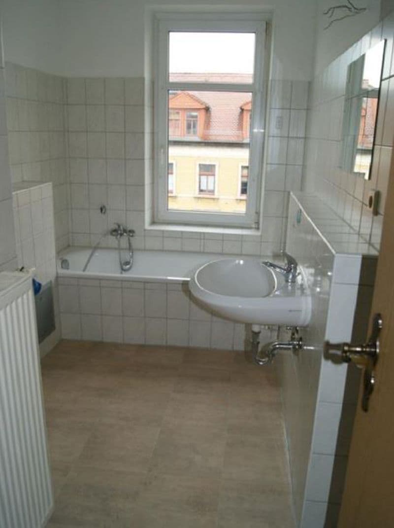 Badezimmer mit Wanne, rundem Waschtisch, weißen Fliesen bis Hüfthöhe, Fenster mit Blick auf Nachbargebäude