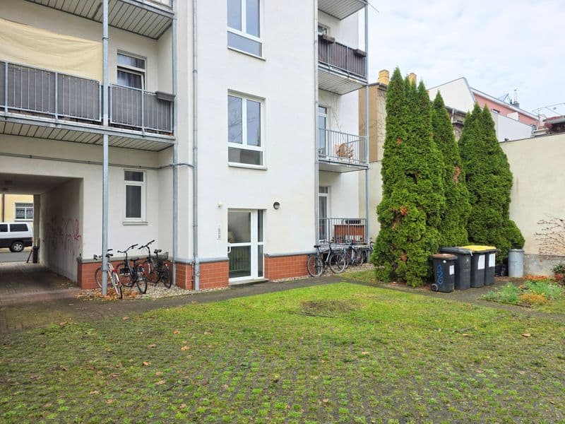 Mehrgeschossiges Wohngebäude mit weißer Fassade, rotem Sockel, Balkonen und großer Grünfläche mit efeuberanker Wand
