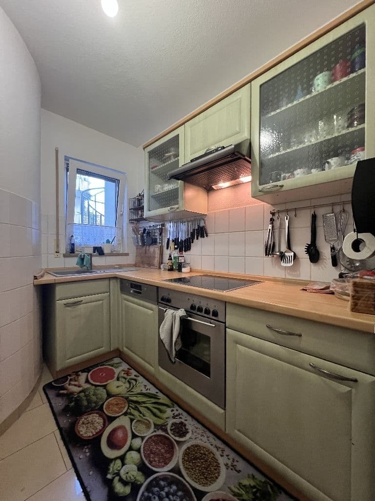Kleine Küche mit hellgrünen Unterschränken, Holzarbeitsplatte, weißen Wandfliesen, Fenster zur Straße