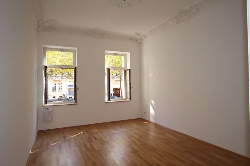 Leeres Zimmer mit Parkett, zwei Fenster mit Stuckdecke, Heizkörper an der Wand