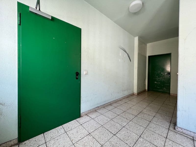 Flur mit grüner Eingangstür, Fliesen, weißen Wänden und weiterer Tür im Hintergrund