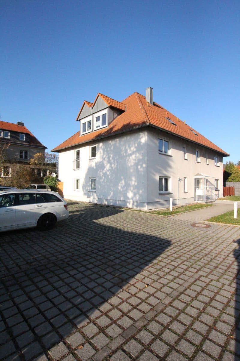 Zweistöckiges Wohnhaus mit Mansardendach und Ziegeln, weiße Putzfassade, Gauben mit Dachfenstern, gepflasterte Zufahrt
