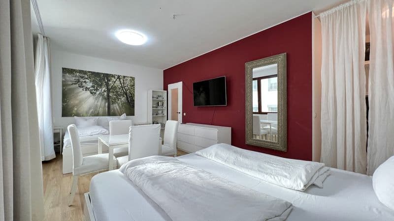 Schlafzimmer mit zwei Einzelbetten, weinroter Akzentwand, TV-Gerät, Spiegel, Parkettboden, Essbereich mit Tisch und Stühlen