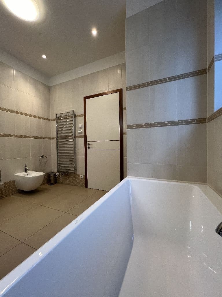Badezimmer mit weißer Badewanne im Vordergrund, beige Wandfliesen mit Bordüre, Waschbecken