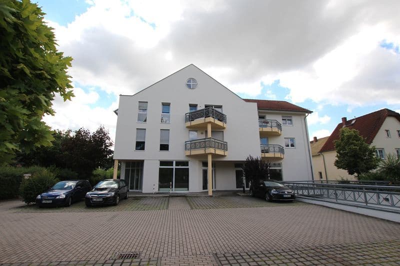 Viergeschossiges Wohnhaus mit weißer Fassade, Satteldach, zwei Balkonen und Erdgeschoss-Ladenzeilen