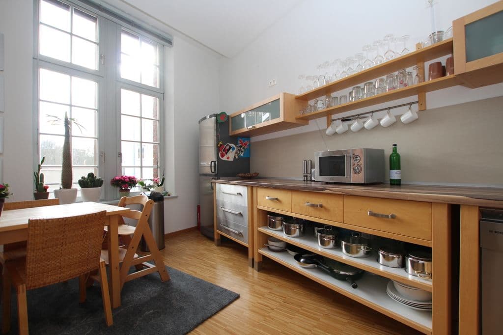 Wohnküche mit Holzmöbeln, offenen Regalen, Esstisch am Fenster, Parkettboden, helle Wände