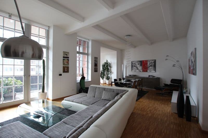 Offenes Wohnzimmer mit großzügigen Fenstern, modernem Ecksofa, Holzparkett, Balkendecke und Designleuchte