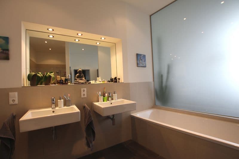 Badezimmer mit zwei Waschbecken, großem beleuchteten Spiegel, Badewanne und Wandfliesenpaneel