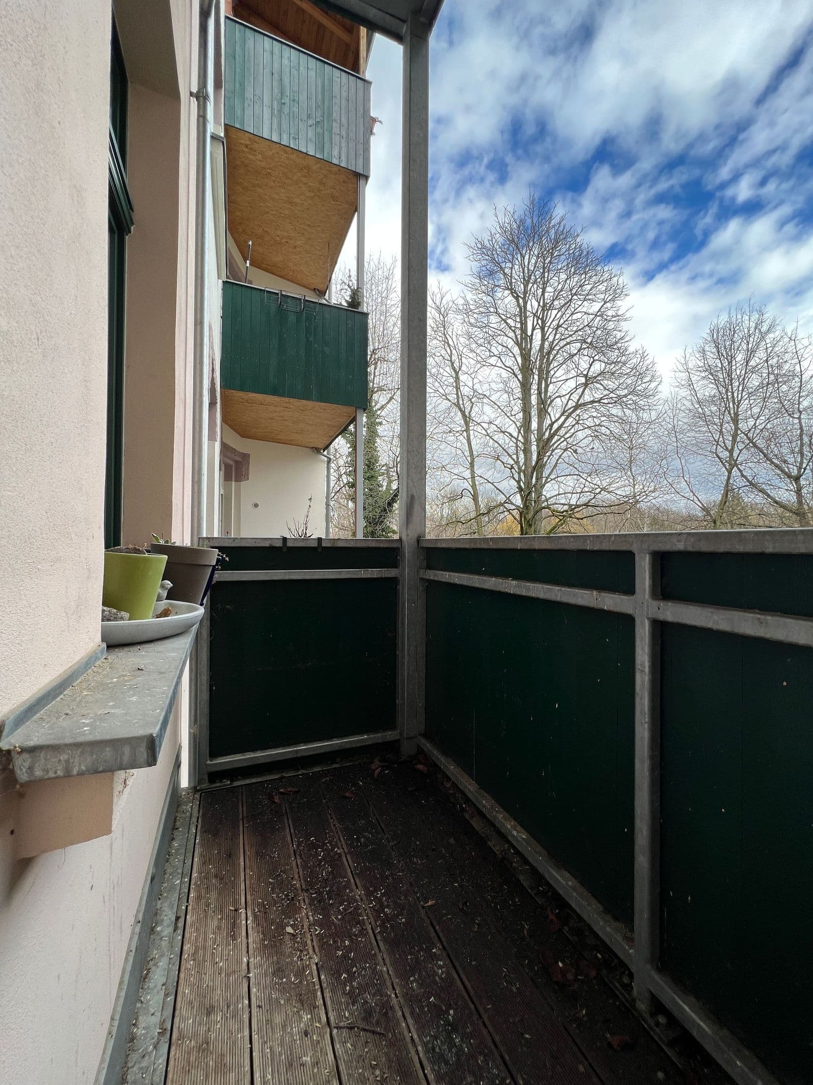Balkon mit dunklem Holzbelag, grünem Sichtschutz, Blick auf Wohngebäude mit Balkonen und kahle Bäume