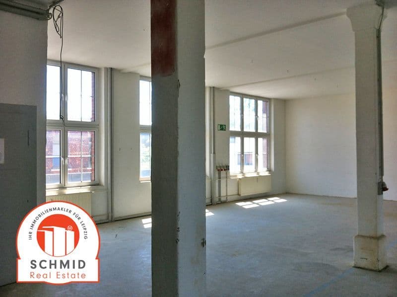 Leerer Raum mit Betonestrich, zwei Stützpfeiler, großflächige Fenster, helle Wände