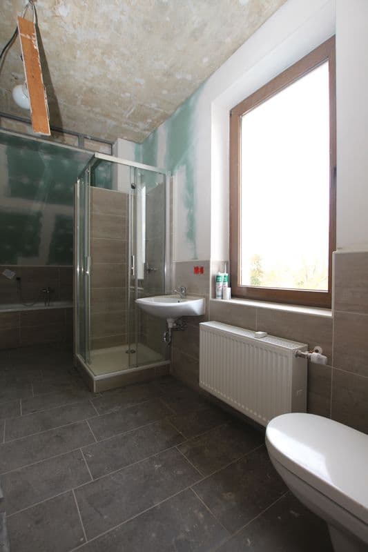 Badezimmer mit Duschkabine, Waschtisch, Toilette, Fliesen, Fenster mit Holzrahmen