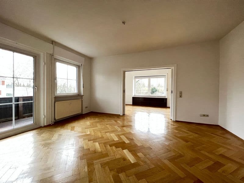 Wohnzimmer mit Herringbone-Parkett, hellen Wänden, großem Fenster zur Terrasse und Durchgang zu Nebenzimmer