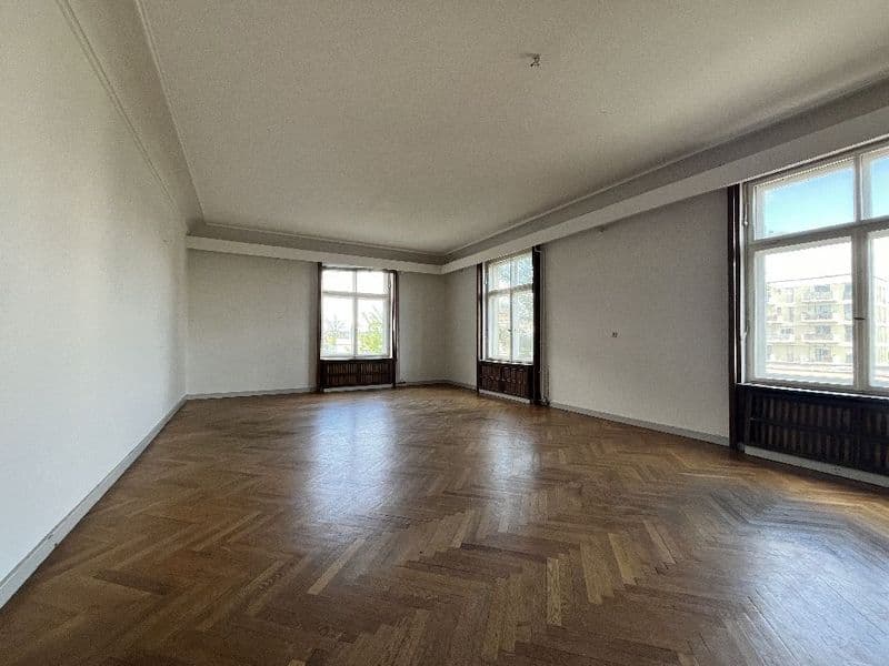Leerer Wohnraum mit Fischgrät-Parkett, heller Decke mit Stuckleisten, drei großen Fenster und Heizkörpern
