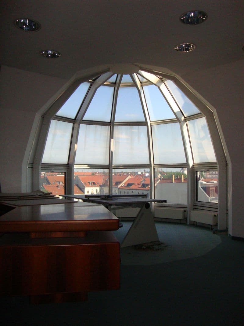 Kuppelförmiger Raum mit Rundfenstern, Blick auf Dächer mit roten Ziegeln, Betonboden, Holzmöbel