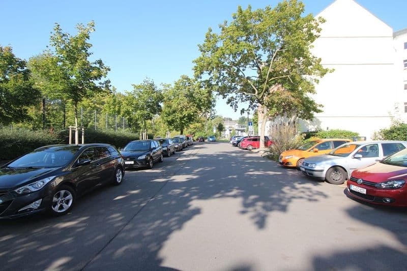 Parkplatz mit geparkten Autos, großen Bäumen und weißem Wohngebäude rechts, Elisenstraße in Chemnitz