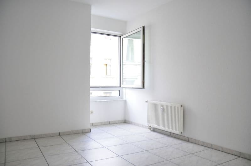 Leeres Zimmer mit Fliesenboden, weiße Wände, Heizkörper, geöffnetes Fenster
